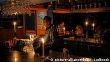 Drei Menschen sitzen bzw. stehen in einer Bar, die mit Kerzen beleuchtet wird