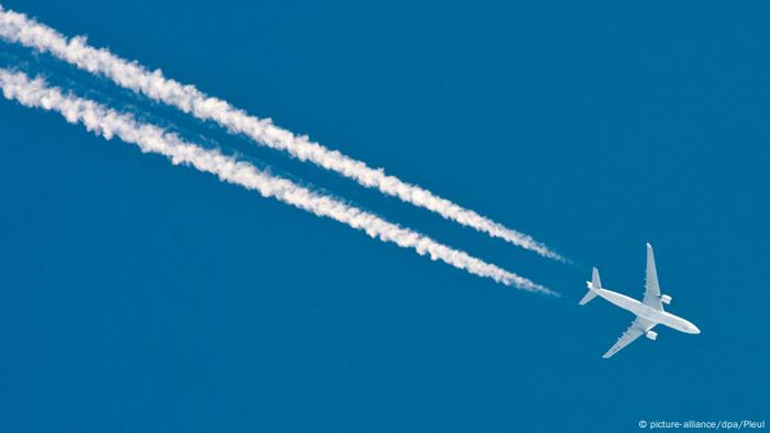 A plane streaks across a deep blue sky, leaving white lines in its wake