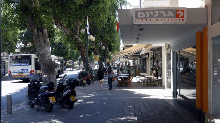 Tree-lined street, shops, people, outdoor cafes, a few pedestrians