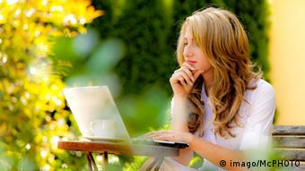 Девушка сидит с ноутбуком за столиком в осеннем саду