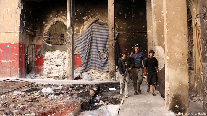 Inmitten eines zerbombten Hauses läuft ein Mann mit zwei Jungen im Arm. Alle Drei haben Maschinengewehre in der Hand. (Foto: Fadi al-Halabi/AFP/Getty Images)