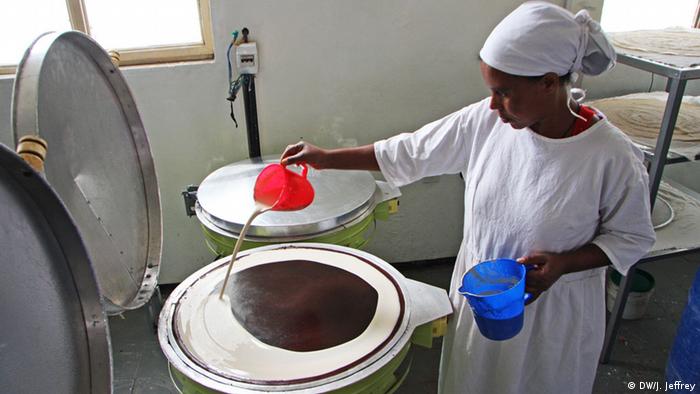 A woman pouring a fermented mixture of teff flower and water onto a clay-surface stove to make injera