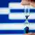 An hour glass in front of a Greek flag.