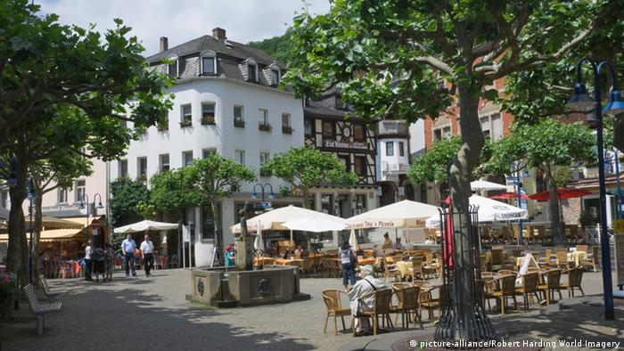 view of square with trees, tables, chairs and open umberllas in Idar-Oberstein, Germany.