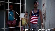 Juan Luis Aldein, 30, wearing a muscle shirt with an American national flag motif, poses with his daughter and his wife, at the front gate to his home, in Havana, Cuba, Wednesday, Feb. 25, 2015. Juan, who is unemployed, expects this new stage of relations between the United States and Cuba will give his family a chance to improve their lives. (AP Photo/Ramon Espinosa)