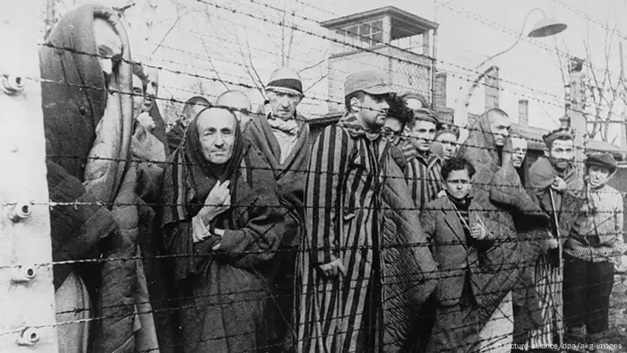 Haggard prisoners stand huddled behind barbed wire in a Holocaust concentration camp (picture-alliance/dpa/akg-images)