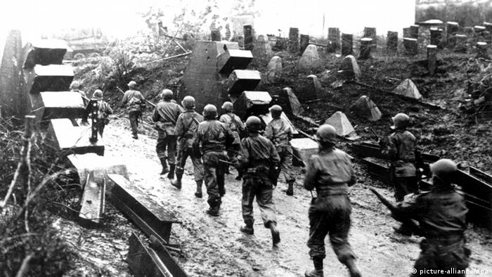 US-amerikanische Soldaten mit Helmen und Gewehren in der Hand durchqueren eine Trümmerlandschaft (picture-alliance).