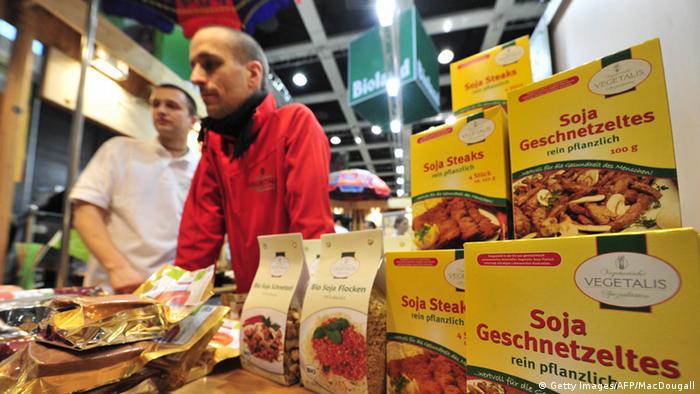 A salesman in Germany stands before a counter where boxes of soy-products are placed to attract customers