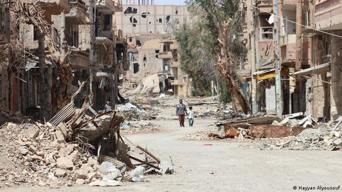 A man walks through a destroyed city holding a little boy by his hand.