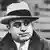 Al Capone em foto preto-e-branca de 1931, com casacão e chapéu, camisa e gravata 