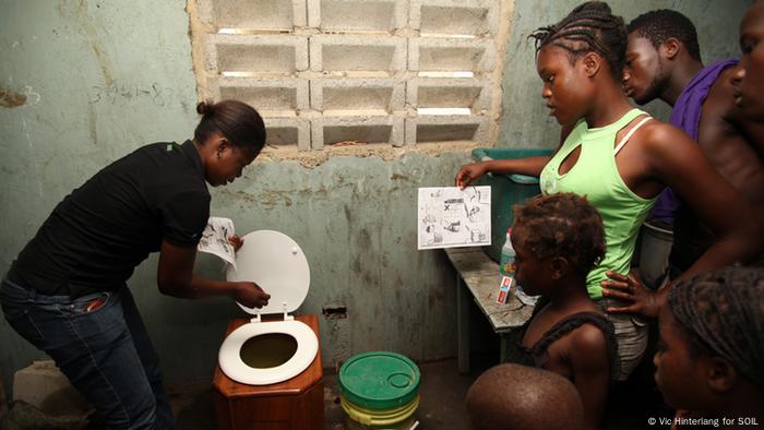 Menschen stehen neben einer Trockentoilette (Photo: Vic Hinterlang for SOIL)