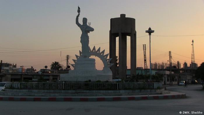 تمثال على شكل امرأة تحمل شعلة بيدها اليمنى، وفروعا في يدها اليسرى. هذا التمثال في المنطقة الكردية بسوريا كان أصلا لحافظ الأسد قبل أن يتم تحويله إلى هذا الشكل. 