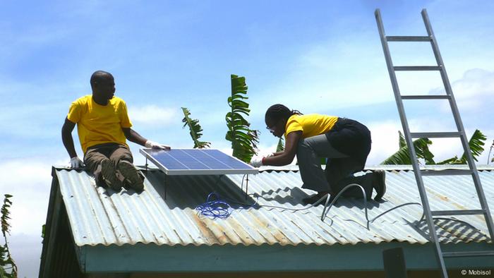 A man and a woman install a solar panel atop a home in Tanzania