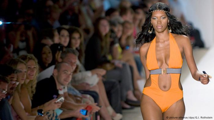 Woman in bright orange one-piece walking down a catwalk