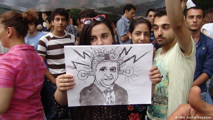 Женщина держит в руках плакат с шаржем на президента Армении