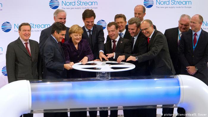 Zwölf Offizielle aus Politik und Wirtschaft öffnen symbolisch ein großes Schraubrad zur Inbetriebnahme der Pipeline Nord Stream. An der Rückwand mehrere Aufschriften Nord Stream - The new gas supply route to Europe neben dem Firmenlogo von Nord Streaam