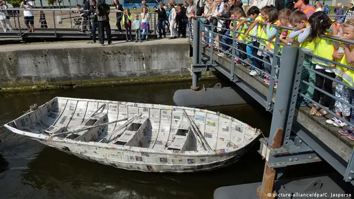 Kinder beobachten am Hafenbecken in Bremerhaven wie ein das Papierboot über das Wasser gezogen wird. Foto: (dpa)