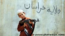 epaselect epa04868675 A picture made available on 01 August 2015 shows an unidentified child from a militant of Islamic State (IS) playing with an AK-47 rifle as the text on the wall reads in Arabic 'Islamic State - Khurasan Chapter' at an undisclosed location in Kunar province, Afghanistan, 30 July 2015. More than 1000 Afghan families have been displaced by clashes in the Achin and Spinghar districts in eastern Afghanistan between armed opposition groups, some allegedly claiming allegiance to the group calling themselves the Islamic State (IS) after defecting from the Taliban. EPA/GHULAMULLAH HABIBI