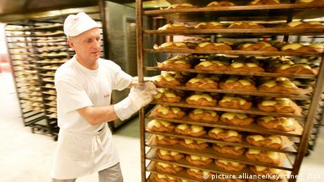 ein Bäcker schiebt einen Wagen voller Bleche mit Puddingteilchen
