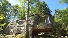 Eine Holzhütte mit organisch runden Formen mitten im Wald. Sie sieht beinahe aus wie eine Schnecke. Das Haus lässt sich auseinander ziehen. 