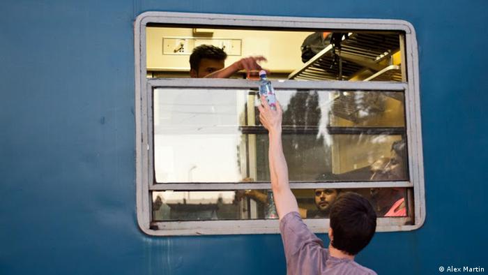 A refugee takes a bottle of water from a volunteer before departure