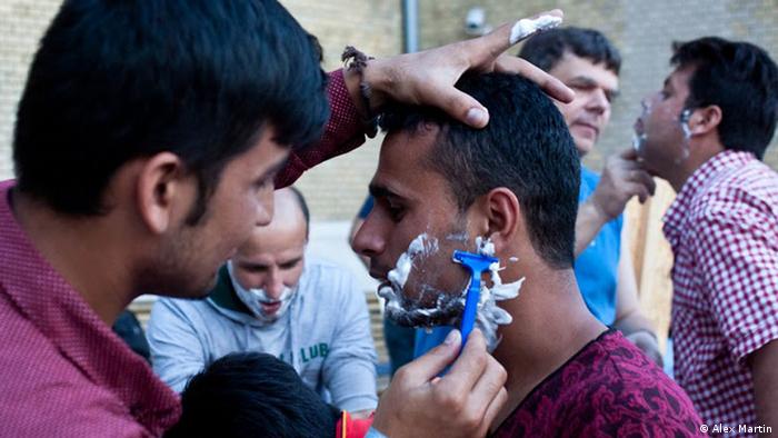 An Afghan man helps shave one of his compatriots at the Szeged train station