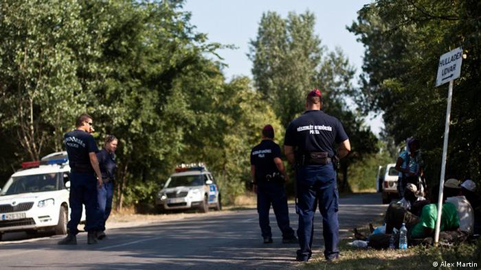 police officers watch over newly arrived migrants at Asotthalom