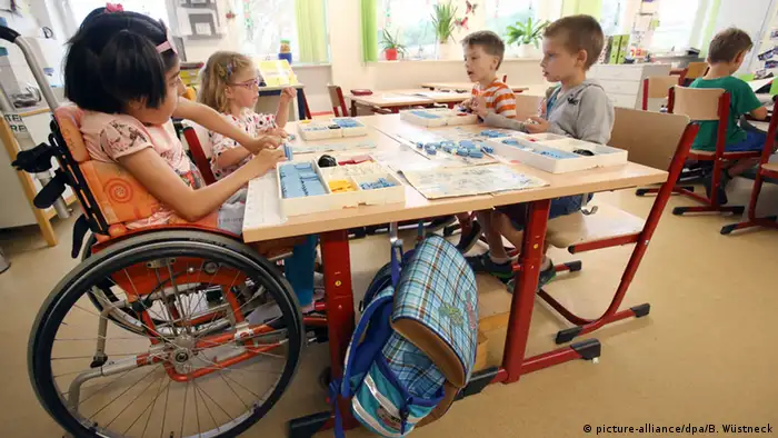Ein Mädchen im Rollstuhl sitzt neben Kindern ohne Handicap (picture-alliance/dpa/B. Wüstneck)