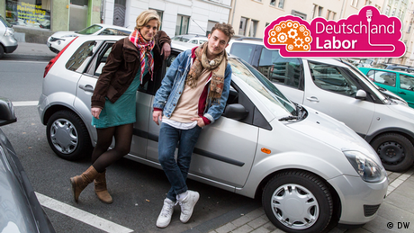 Eine junge Frau und ein junger Mann posieren vor einem Auto.