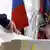 Человек бросает бюллетень в избирательную урну, которая стоит рядом с флагом РФ