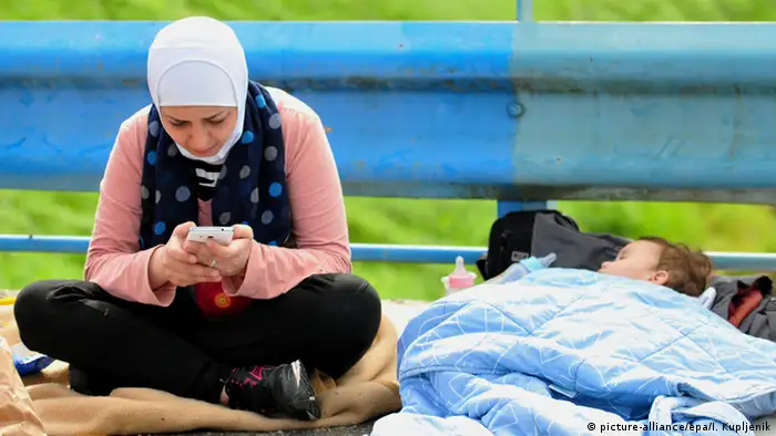 Woman sits looking at her phone with a child sleeping beside her