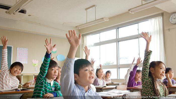 School children raise their hands in class.