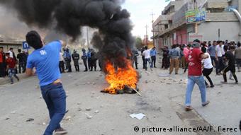 Junge Kurden, die Steine werfen. In der Mitte der Straße brennt ein Feuer.