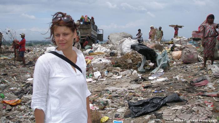 A woman stands in front of a pile of trash