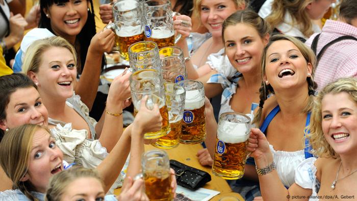 Las mujeres que visten dirndls sonríen y sostienen sus jarras de cerveza.