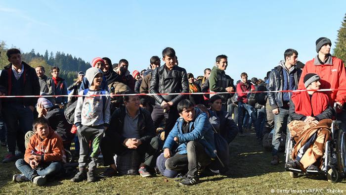 Беженцы ожидают разрешения на проход в Германию, сидя и стоя на траве возле границы