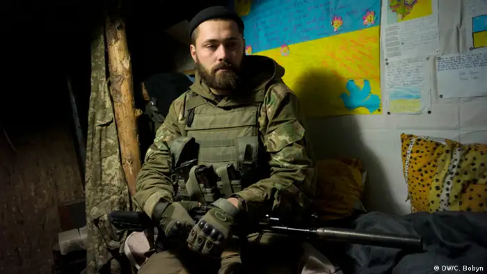 Maxim sits on his bed in an underground earth and wood bunker on the frontline