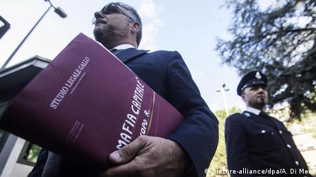 Law suit begins against the mafia: man carrying a file, with a policeman to the side (Photo: picture-alliance/dpa/A. Di Meo)