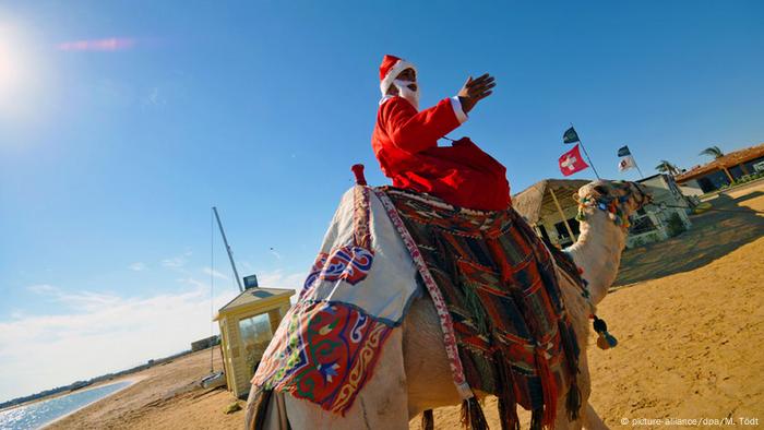 A resort employee disguised as Santa Claus rides a camel along the beach, Egypt.