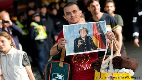 Ein Flüchtling, der kurz zuvor mit einem Zug angekommen ist, läuft am 05.09.2015 auf dem Hauptbahnhof in München (Bayern) über den Bahnsteig und hält dabei ein Foto von Angela Merkel in den Händen - Foto: Sven Hoppe (dpa)