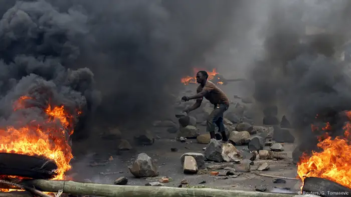 Fires burn as a protester throws rock in Burundi