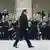 Франсуа Олланд идет вдоль оркестра музыкантов, стоящих на площади