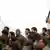 Ein maskierter IS-Kämpfer steht mit gezückten Messer neben einer Gruppe sitzender, gefangener Soldaten der syrischen Armee (Copyright: picture-alliance/AP Photo)
