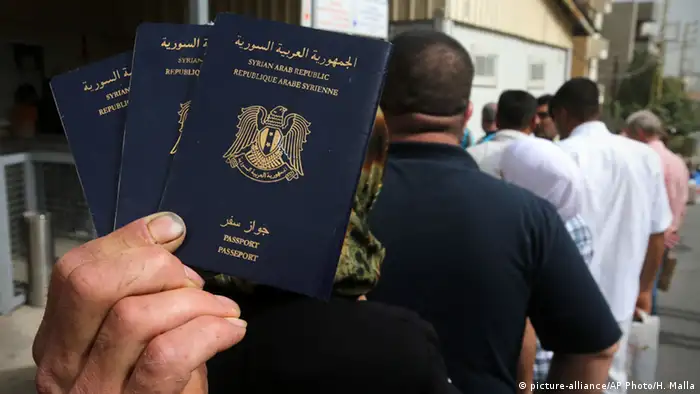 Ein Syrer steht in einer Warteschlange und hält seinen Pass in die Kamera. (Foto: picture-alliance/AP Photo/H. Malla)