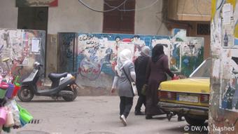 Loose electricty wires dangle over the heads of women walking through Shatila camp.
