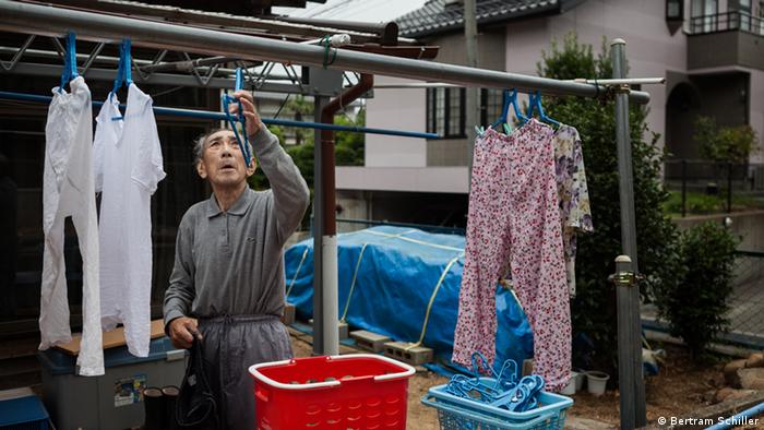 Ein Mann hängt seine Wäsche zum Trocknen auf eine Wäscheleine. Im Hintergrund des Gartens ein Hügel aus kontaminiertem Material, das nur mit einer blauen Plane abgedeckt wurde. (Foto: Bertram Schiller).