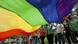 A group of people hold a large, rainbow flag A group of people hold a large, rainbow flag