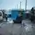 Frankreich Polizei räumt das illegale Flüchtlingslager Jungle bei Calais. Holzbaracken sind notdürftig zusammengehämmert. Durch die schlammige Straße fährt ein LKW mit Plane, auf der Ladefläche fahren Männer mit. (Foto: DW/Diego Cupolo)