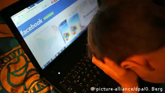 Boy holds his head in front of a laptop screen showing a Facebook page.