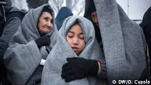 Migrants wrapped in grey felt blankets